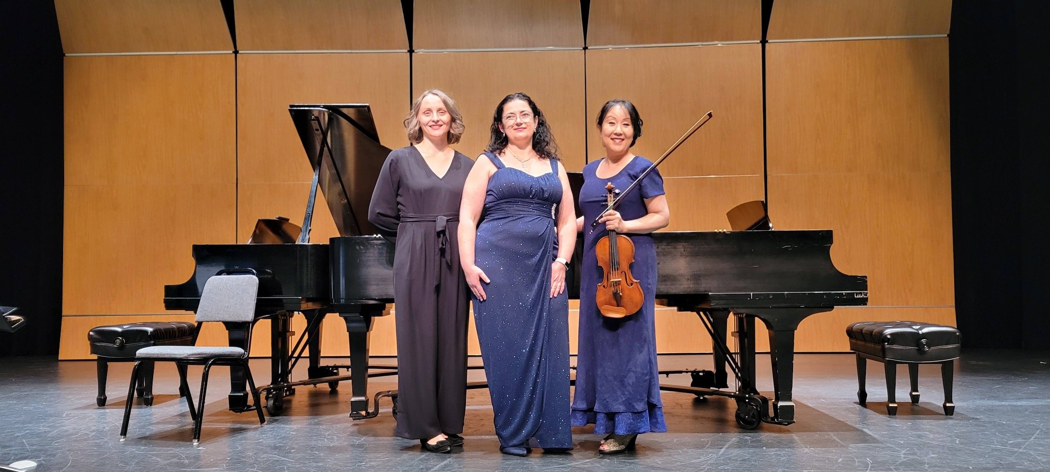 Dr. Alina Kirshon-Goldman performing on stage in concert attire with collaborating musicians and grand pianos